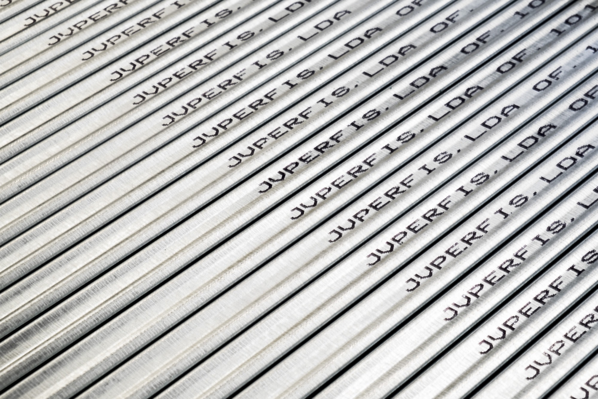 Close-up of galvanised profiles on the diagonal, each carrying the printed mark “JVPERFIS, LDA OF. 10” repeated along the steel.